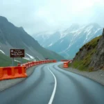 Route sinueuse du Col du Petit Saint-Bernard avec des barrières de chantier et des plaques de neige printanière sur les versants alpins